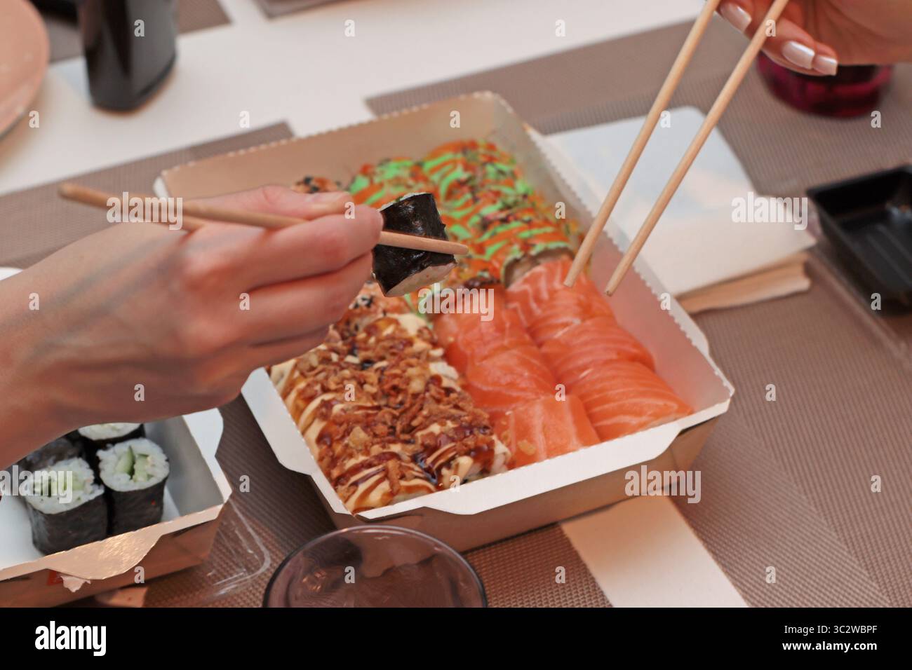 Un invitante shot di sushi roll disposti elegantemente su un tavolo. Mani delicate con bacchette, che mettono in mostra l'arte della cena. Nelle vicinanze, tovaglioli Foto Stock