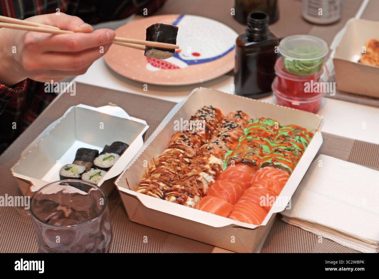 Un invitante shot di sushi roll disposti elegantemente su un tavolo. Mani delicate con bacchette, che mettono in mostra l'arte della cena. Nelle vicinanze, tovaglioli Foto Stock