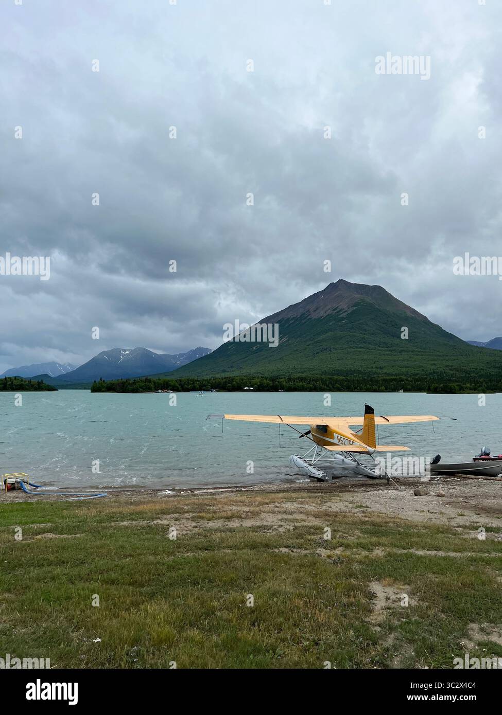 Idrovolante giallo su una sponda remota del lago nel Lake Clark National Park, Alaska, circondato da maestose montagne sotto un cielo nuvoloso. La bellezza selvaggia dell'Alaska - Immagine stock catturata con smartphone