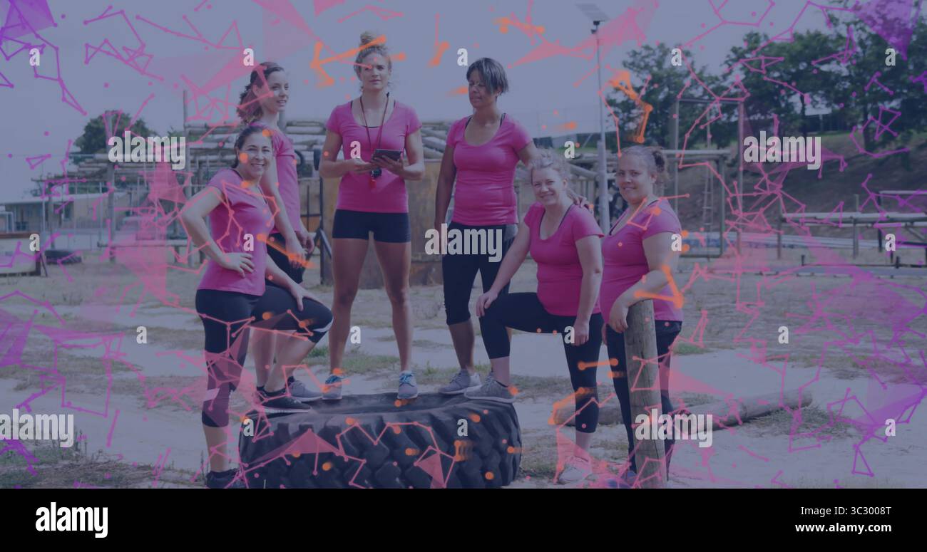 Sei donne in posa con top rosa atletiche appoggiate sulla gomma del trattore in un percorso ad ostacoli, con cronometro Foto Stock