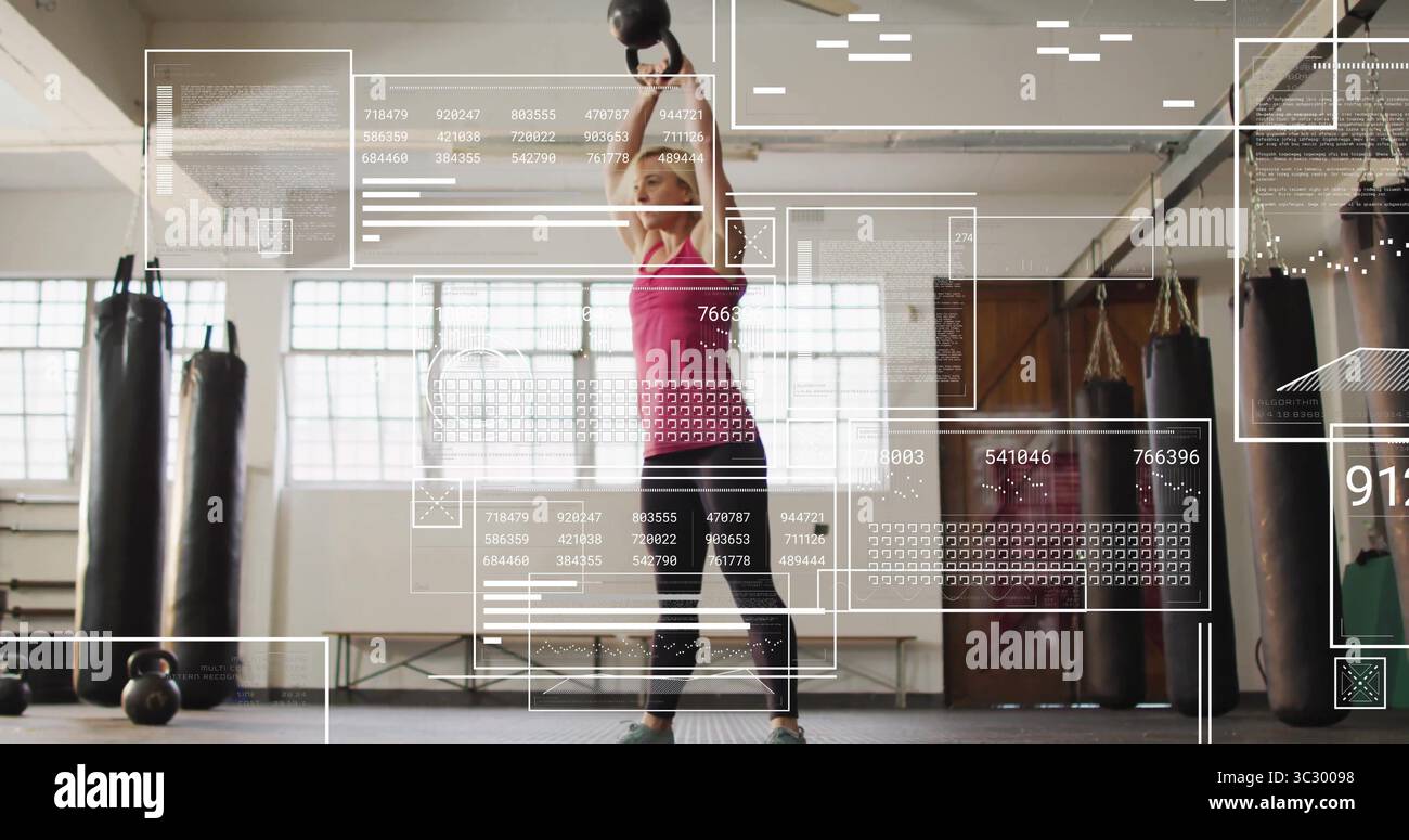 Donna di mezza età in cima rosa che solleva pesanti campanelli in palestra, sacchetti di pugno, sovrapposizioni dati Foto Stock