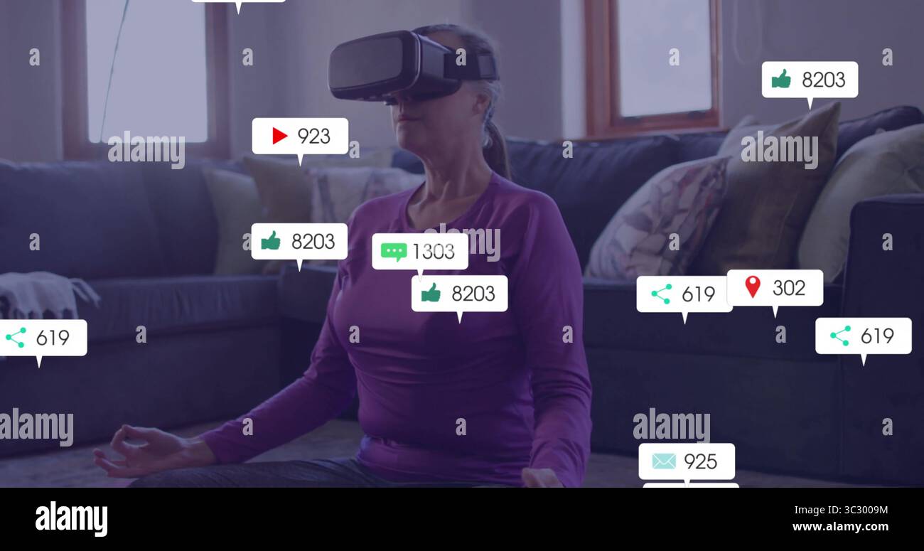 Una donna matura seduta che indossa un visore VR che medita in salotto, con icone fluttuanti dei social media Foto Stock