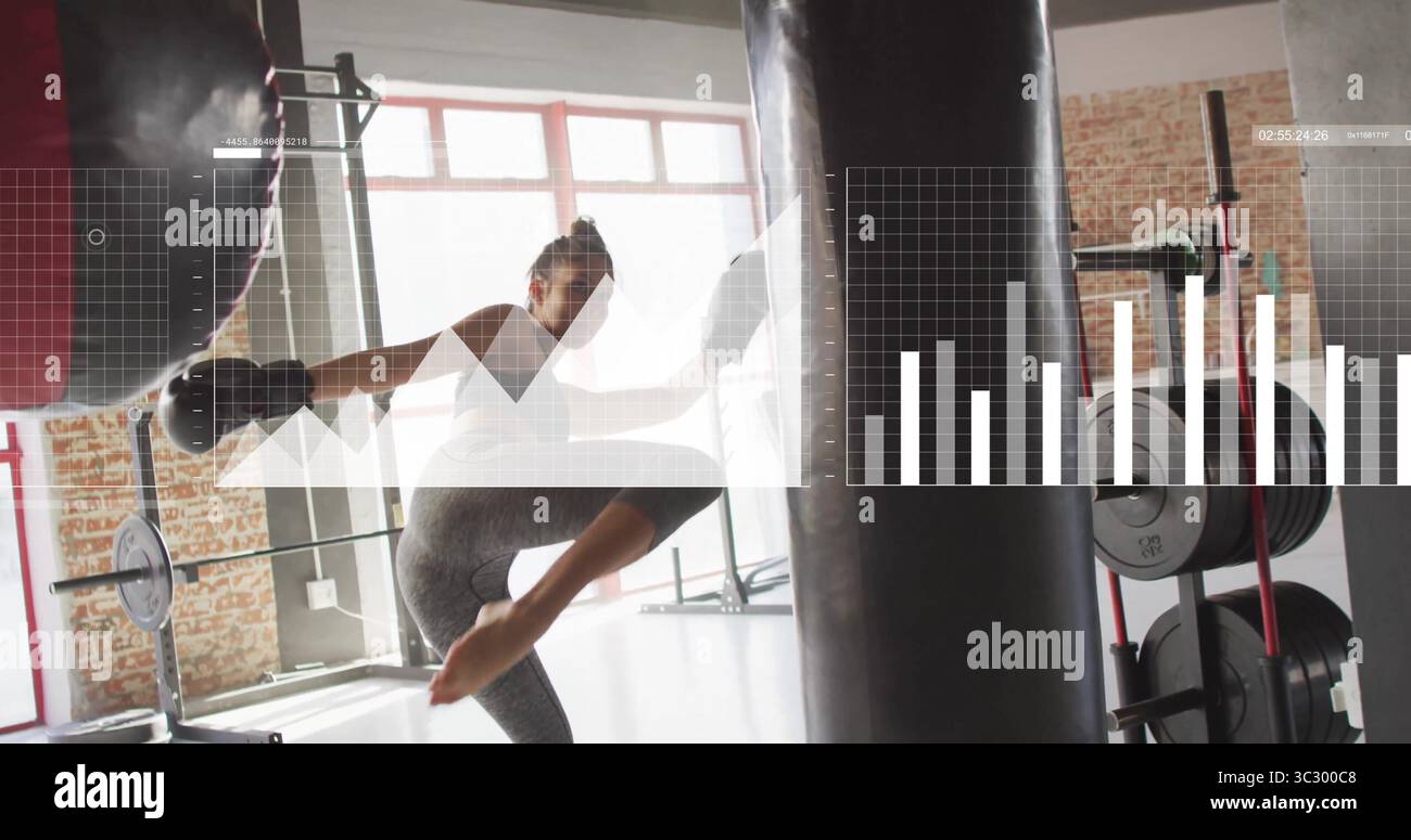 Donna con leggings grigi, guanti neri che calci e pugni una borsa pesante in palestra, con portapacchi Foto Stock