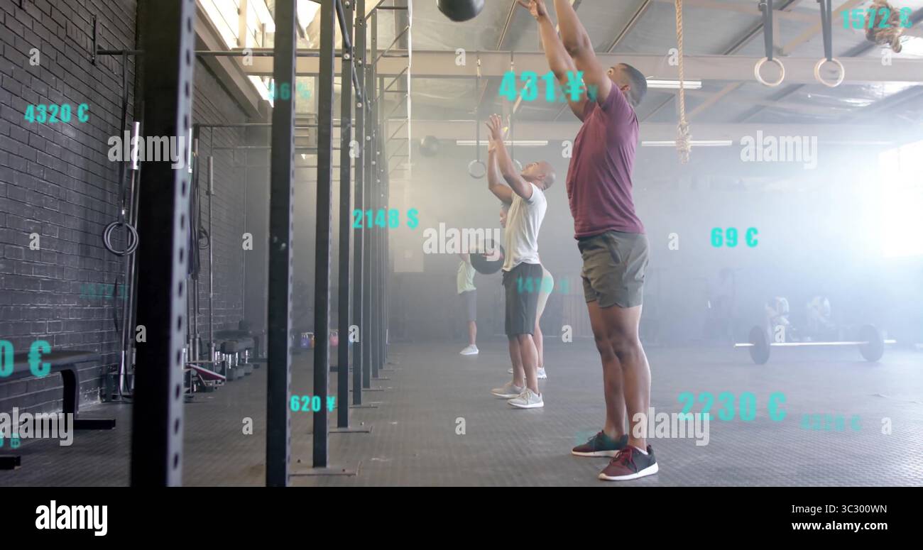 Uomo che indossa una camicia e pantaloncini color marrone che lancia una palla medica sopra la testa nella palestra CrossFit, con metriche Foto Stock
