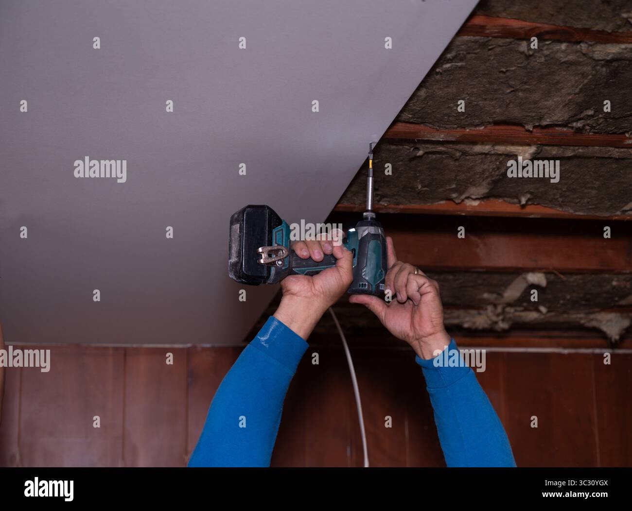 Primo piano delle mani dell’appaltatore che installano pannelli per cartongesso con un trapano e viti durante la ristrutturazione residenziale. Ideale per l'illustrazione delle costruzioni, h Foto Stock