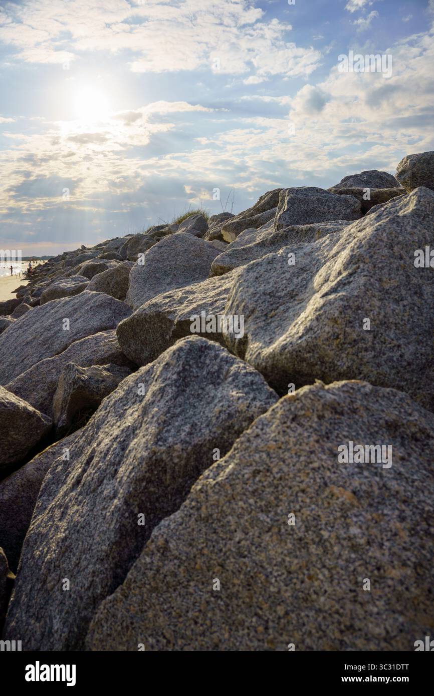 La luce del sole si infrangerà attraverso le nuvole sulle grandi rocce costiere su una spiaggia durante l'ora d'oro. Foto Stock