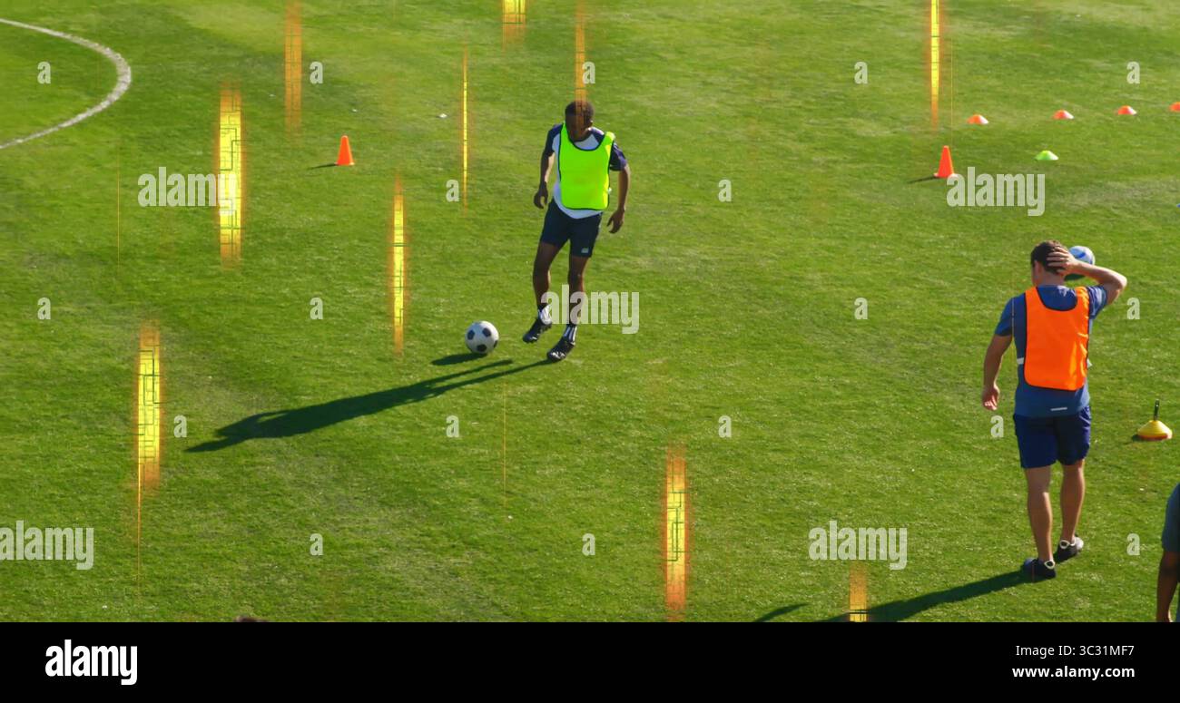 Dribbling di un atleta giallo che controlla la palla da calcio sul campo in erba, con coni arancioni e verdi Foto Stock