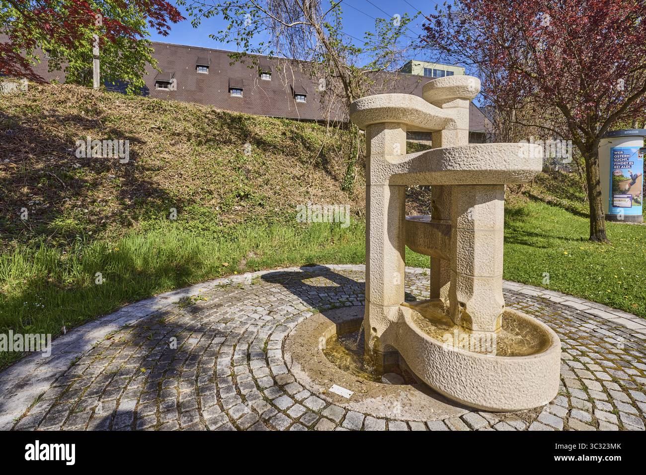 Fontana in pietra, fontana, ciottoli, alberi, prato, Blue Sky, Cloudless, Anton-Winkler-Strasse, Bad Reichenhall, District Berchtesgadener Land, BAV Foto Stock