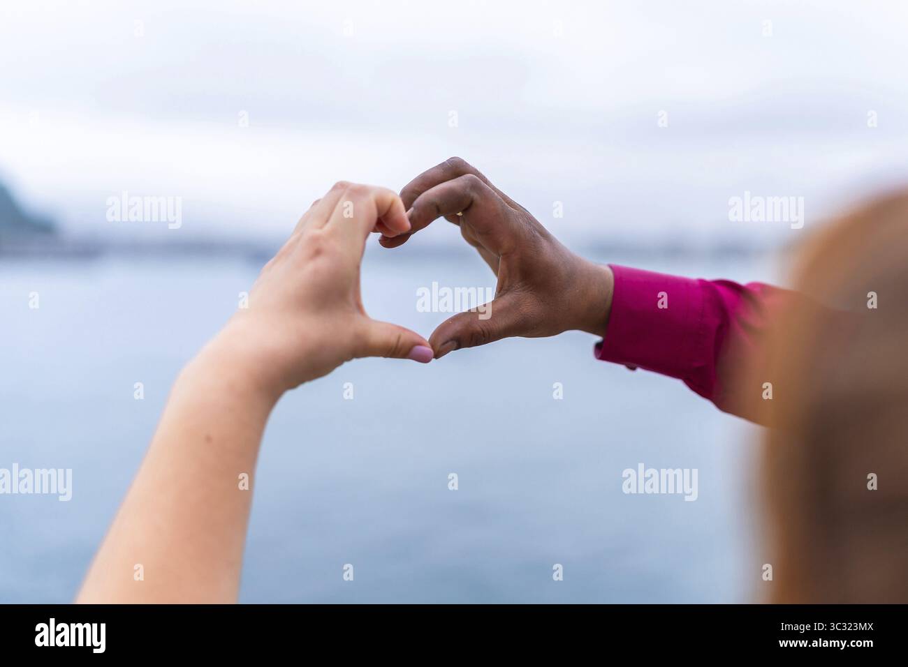 Sposa e sposo che si formano a forma di cuore con le mani contro uno splendido paesaggio marino, celebrando l'amore e l'unità il giorno del loro matrimonio Foto Stock