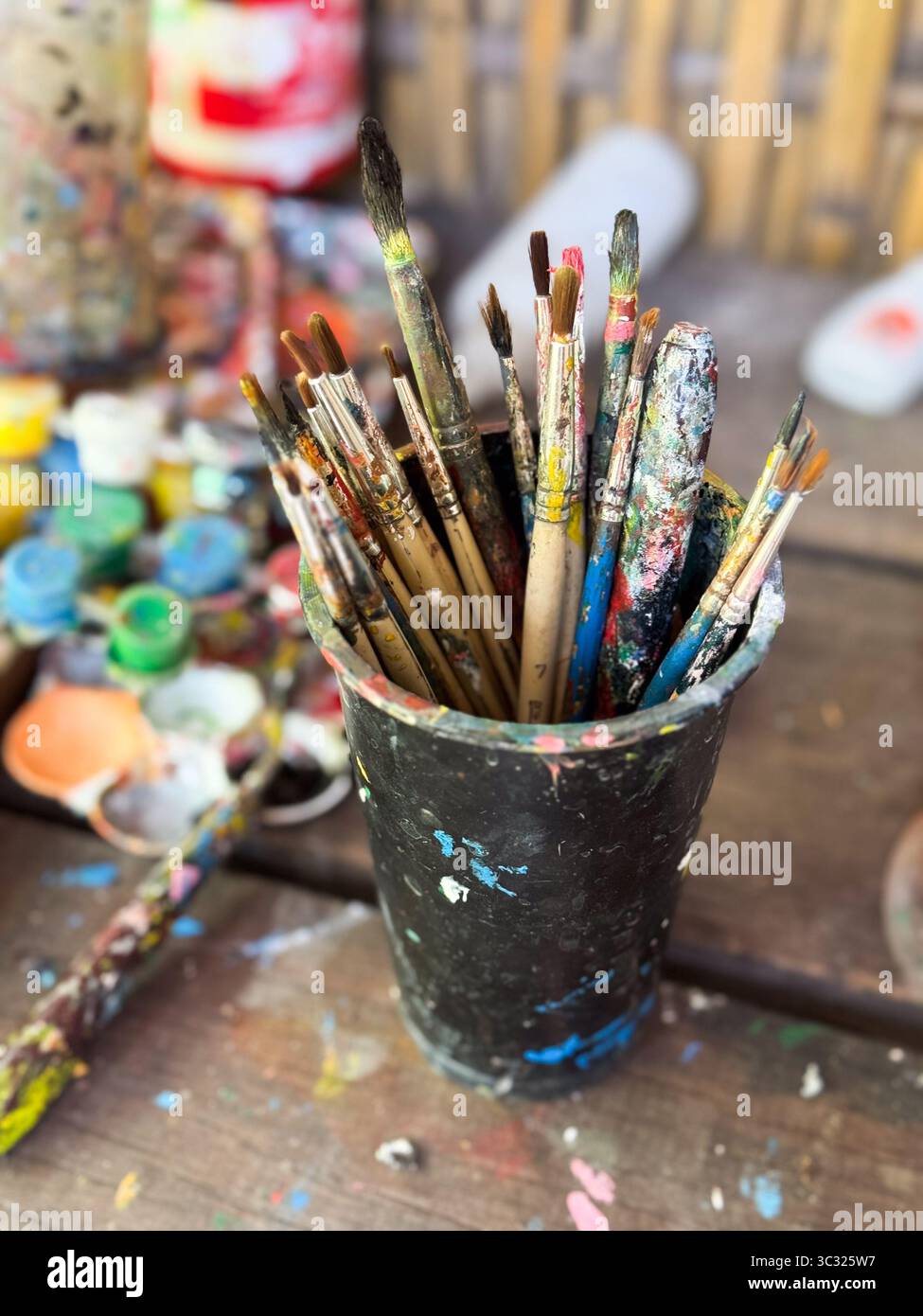 Colorata tavolozza di artisti con vivaci spruzzi di vernice e pennelli su un tavolo di legno. Tavolo dell'artista disordinato. Foto Stock