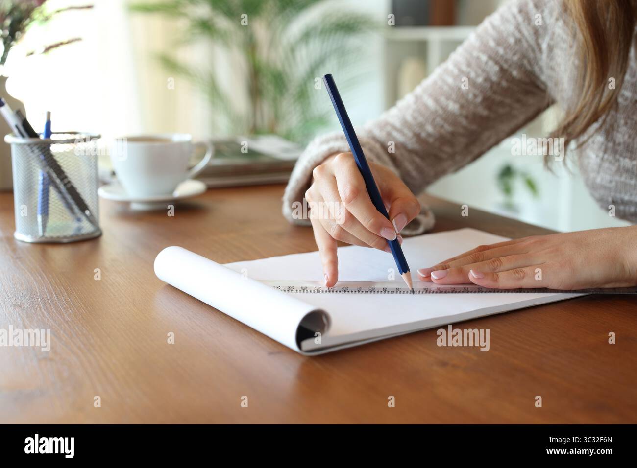 Primo piano di una donna che usa un righello per disegnare su un notebook su un tavolo di legno a casa Foto Stock