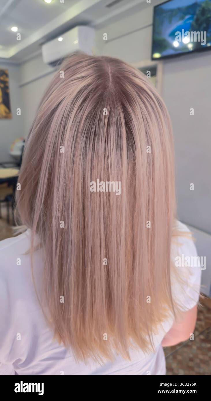 Donna con lunghi capelli tinti leggeri in piedi in un salone di bellezza con schiena. Bionda. Paralume di cenere. Foto Stock