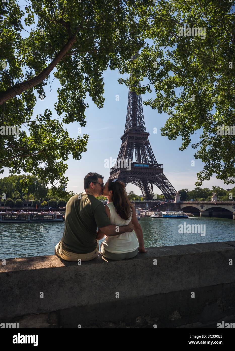 Coppia seduta sul muro che si baciava con la Torre Eiffel in lontananza a Parigi. Foto Stock