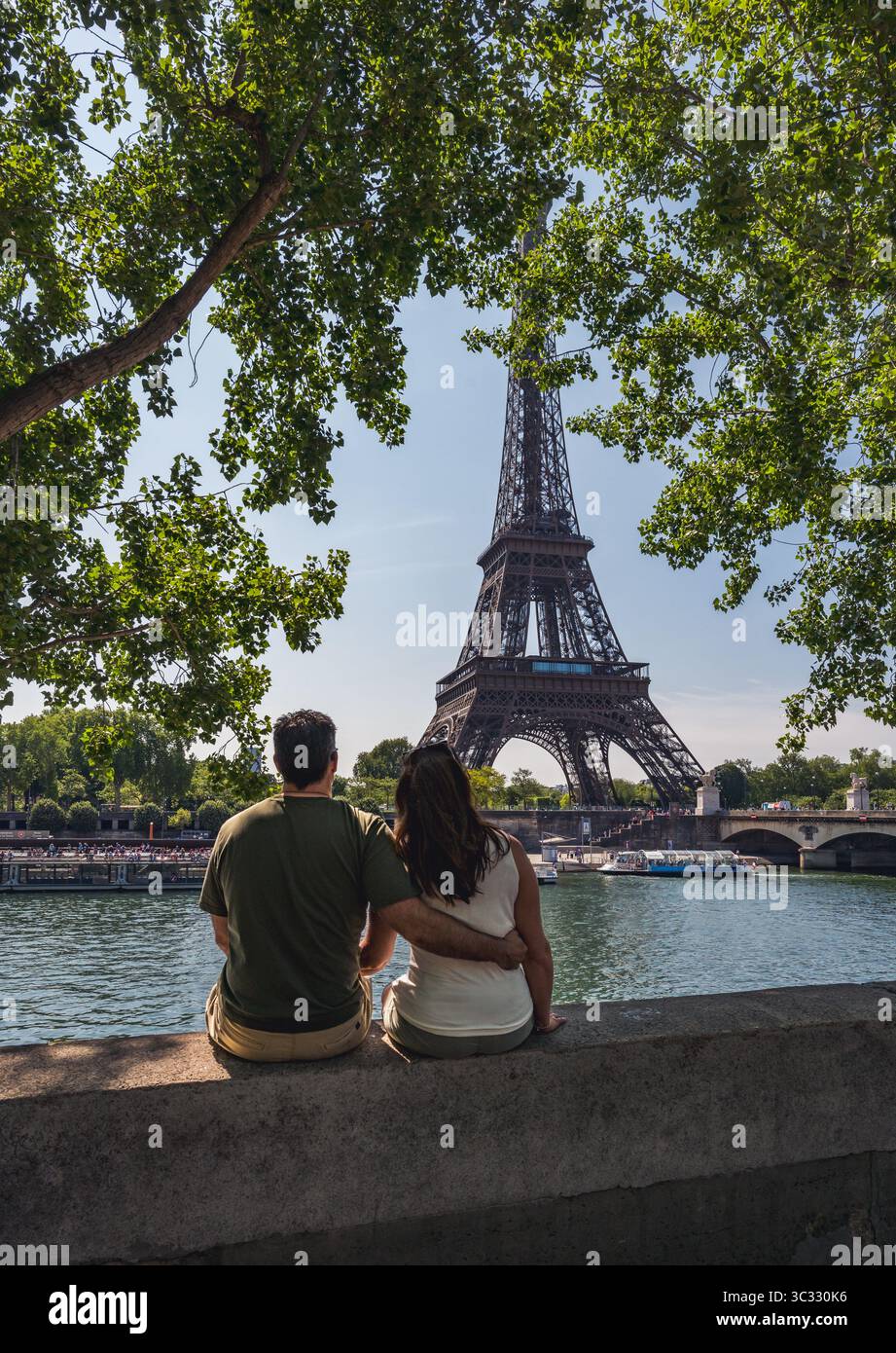 Coppia seduta sul muro che guarda la Torre Eiffel in lontananza a Parigi. Foto Stock