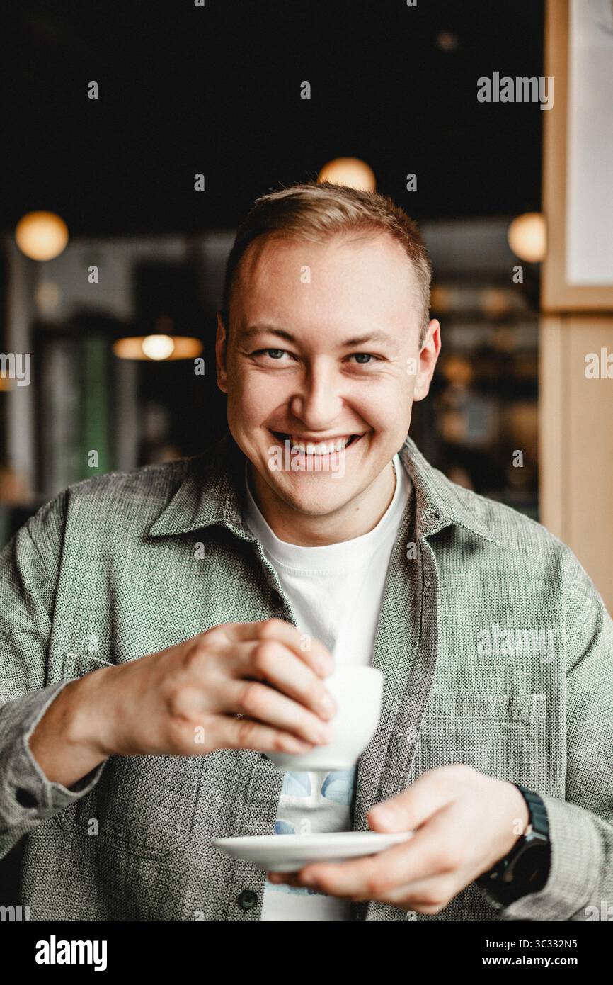 Uomo sorridente che tiene una tazza di caffè in un accogliente caffè Foto Stock