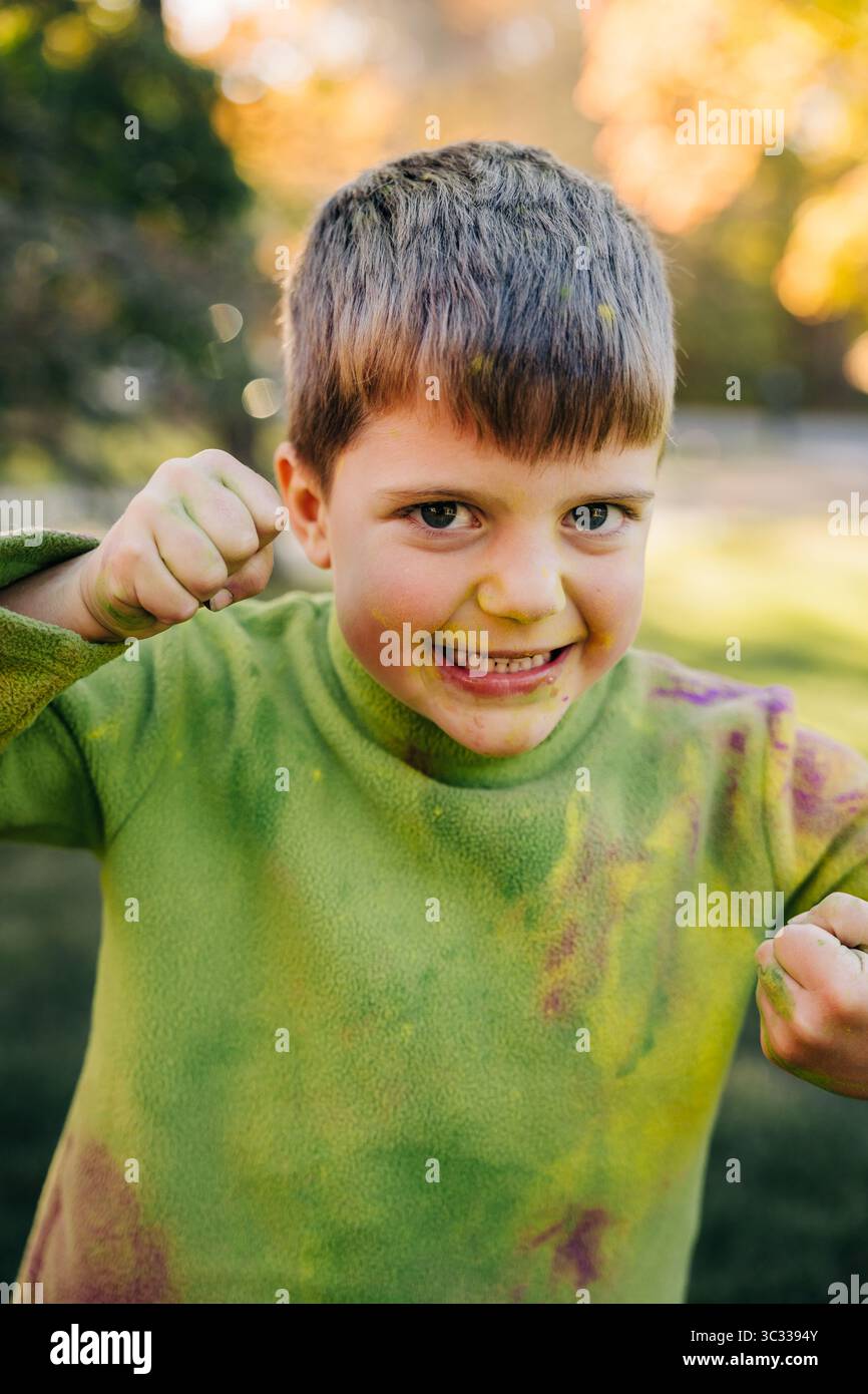 Bambino che gioca e fa facce divertenti ricoperte di colori holi Foto Stock