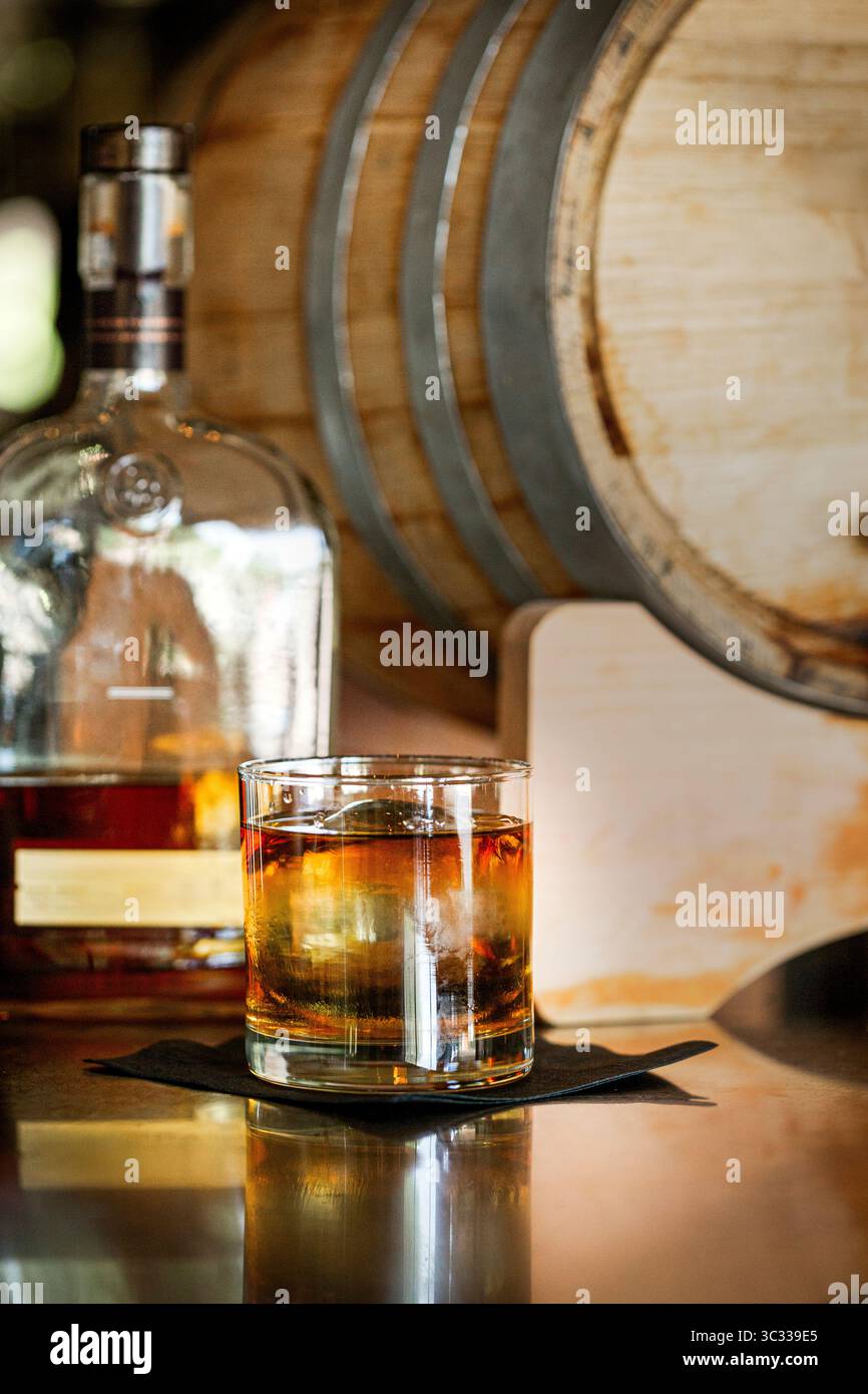 Un bicchiere di whisky su un bar con la bottiglia e un barile di legno Foto Stock