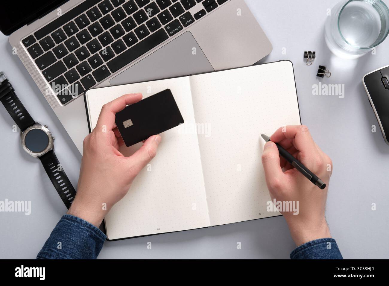 Scrivania con computer, blocco appunti e scrittoio. In una mano un uomo ha una carta di credito, nell'altra una penna. Un posto per il testo. Foto Stock