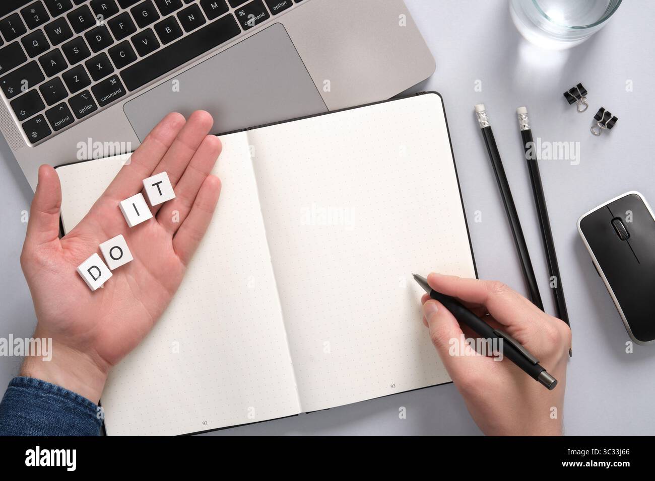 Concetto di motivazione e produttività con un blocco note e didascalia Do IT. Mano che tiene la penna sopra il blocco note vuoto sullo sfondo del desktop. Copyspace Foto Stock