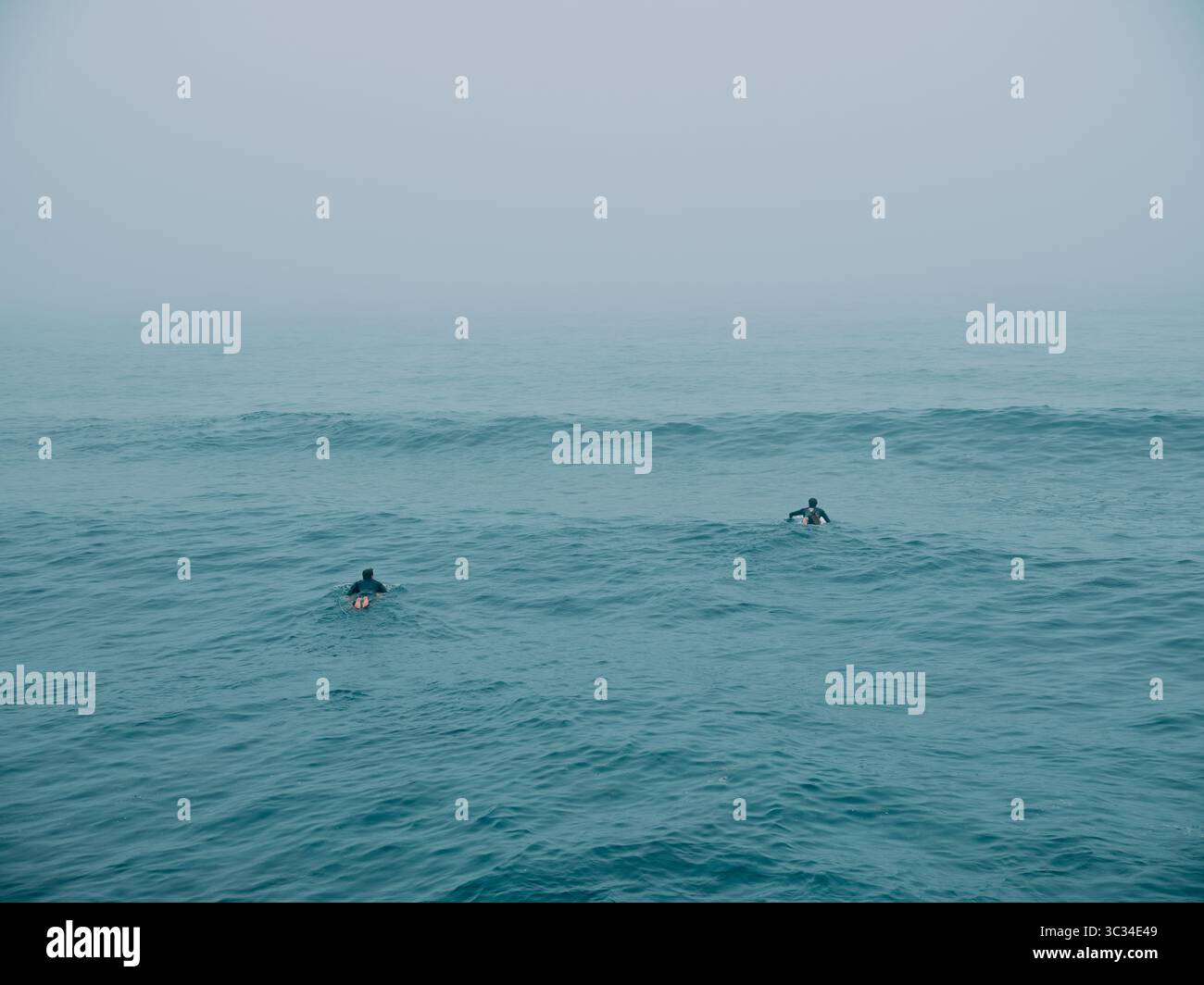 Due surfisti in attesa di catturare un'onda in un mare blu vuoto Foto Stock