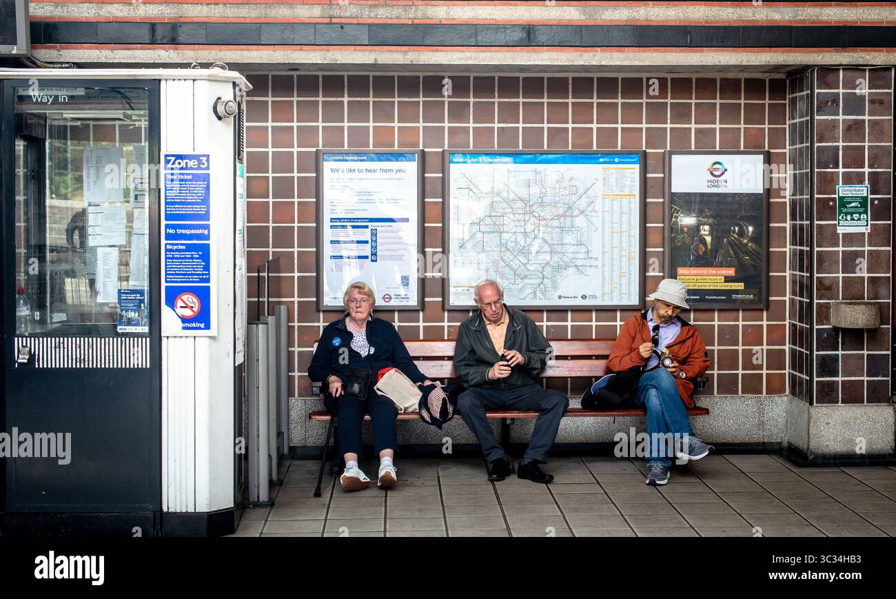Tre passeggeri seduti in panchina nella stazione della metropolitana di Acton Town, Londra, Regno Unito Foto Stock
