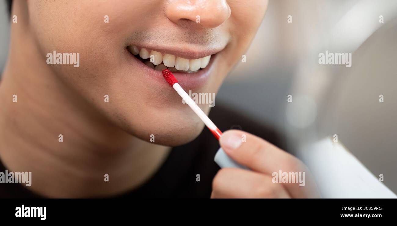 Cura del corpo. Giovane che applica con precisione la lucidatura per labbra rosse. Foto Stock
