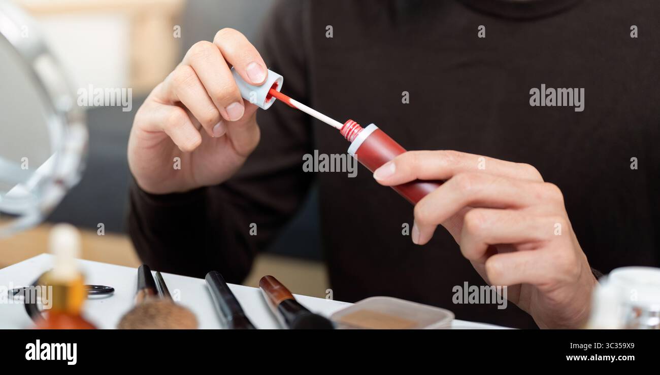 Applicazione di trucco. Primo piano di un maschio che prepara lucidalabbra rossa. Foto Stock