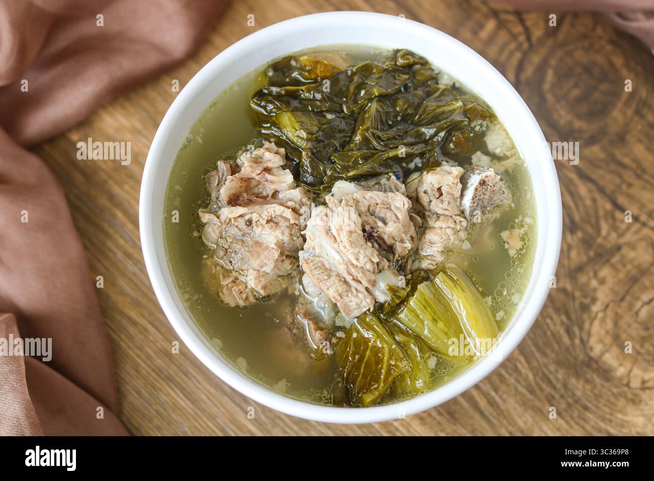 Una ciotola di Bak Kut servita su uno sfondo di legno. Il brodo salato contiene teneri costolette di maiale e grandi pezzi di verdure a foglia verde. Foto Stock