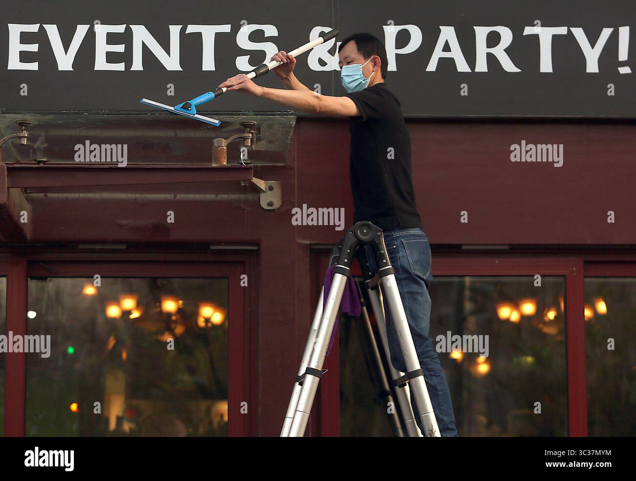 11 aprile 2021, PECHINO, CINA: Un membro del personale cinese indossa una maschera protettiva mentre pulisce l'esterno di un popolare bar occidentale, completamente aperto per gli affari, a Pechino domenica 11 aprile 2021. La capitale cinese ha ridotto l'obbligo di indossare maschere protettive, ad eccezione dei trasporti pubblici, e il distanziamento sociale, mentre la città torna lentamente alla vita pre-covid 19 con ristoranti, aziende e scuole completamente aperti. (Immagine di credito: © Todd Lee/ZUMA Wire) Foto Stock