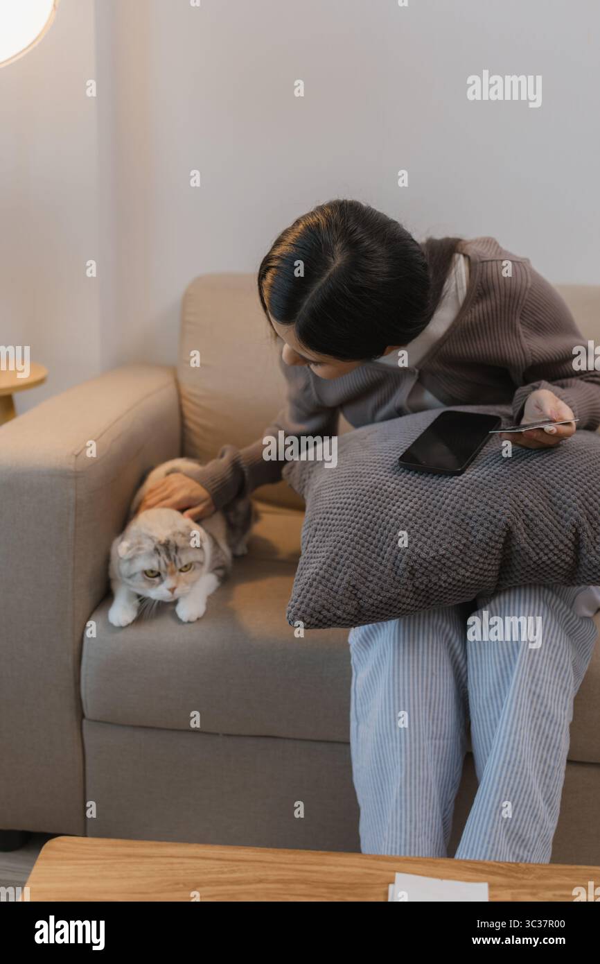 trascorre il suo tempo libero a casa con il suo gatto, lei e il suo gatto si siedono sul divano nel fine settimana dell'appartamento, l'adorabile gatto si siede accanto al suo gufo Foto Stock