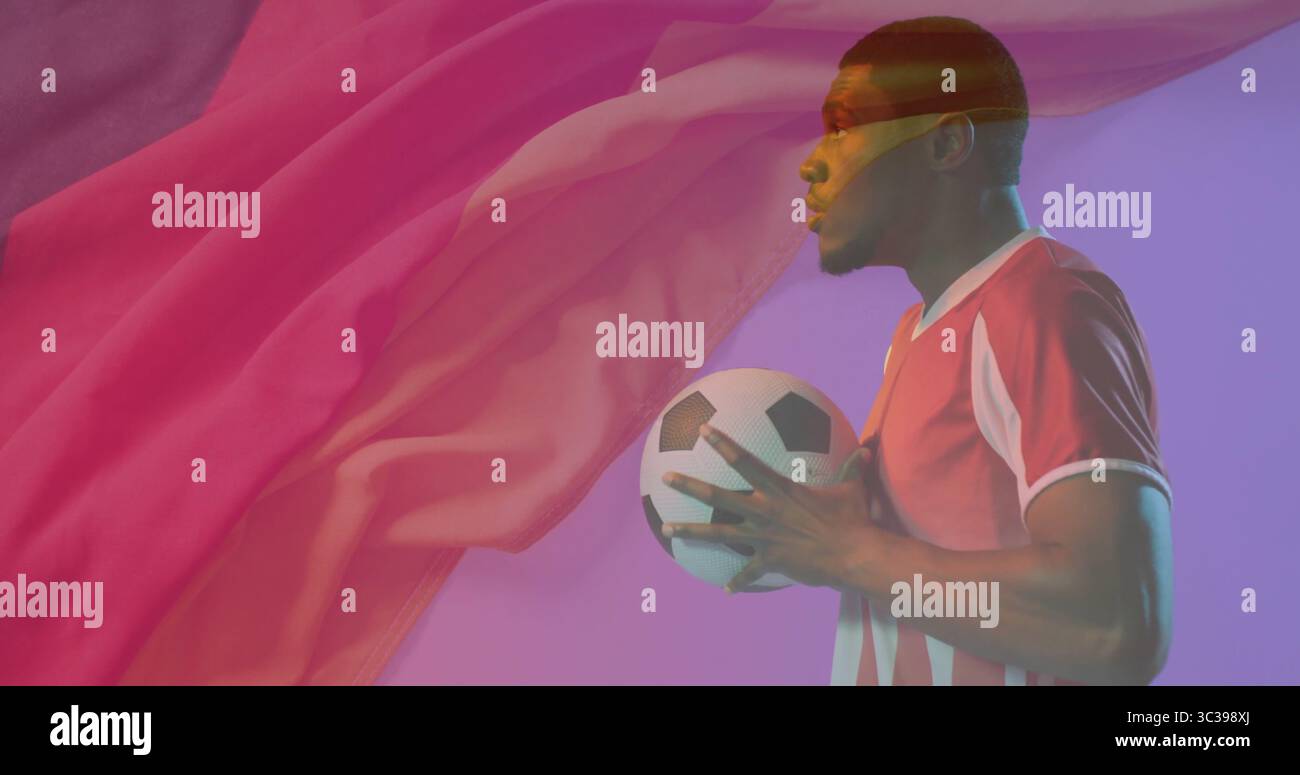 Giocatore di calcio che indossa una maglia rossa che regge la palla da calcio in studio, con tessuto galleggiante, spazio fotocopie Foto Stock