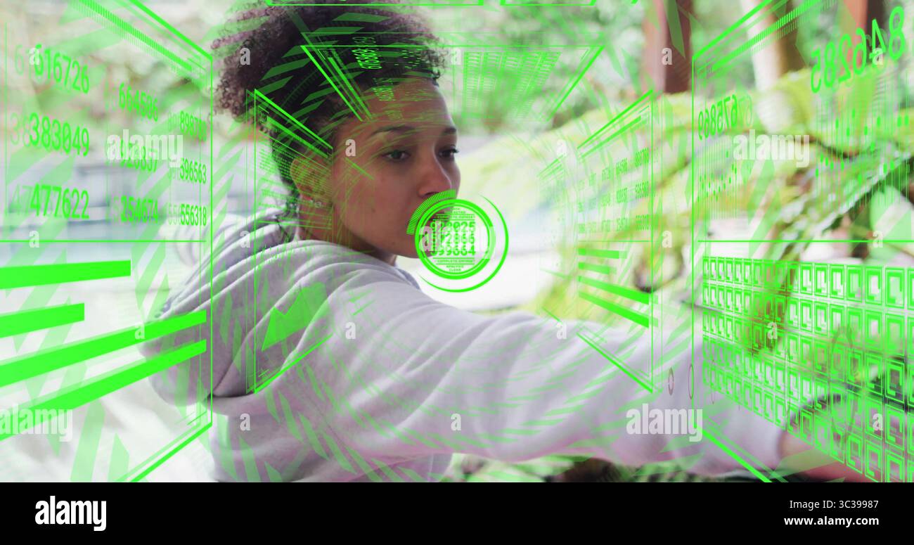 Donna che indossa una felpa con cappuccio utilizzando griglie olografiche in giardino, estendendo il braccio verso i pannelli di codice numerico Foto Stock