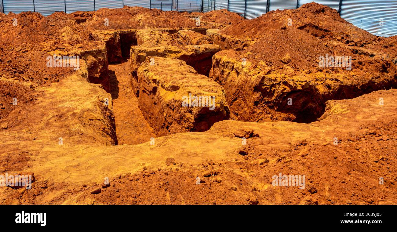 Scavo, fondazioni, con trincee per una grande casa, scavate in terreno rossastro, circondate da pali di sterrato e recinzioni metalliche, sotto il bricco Foto Stock