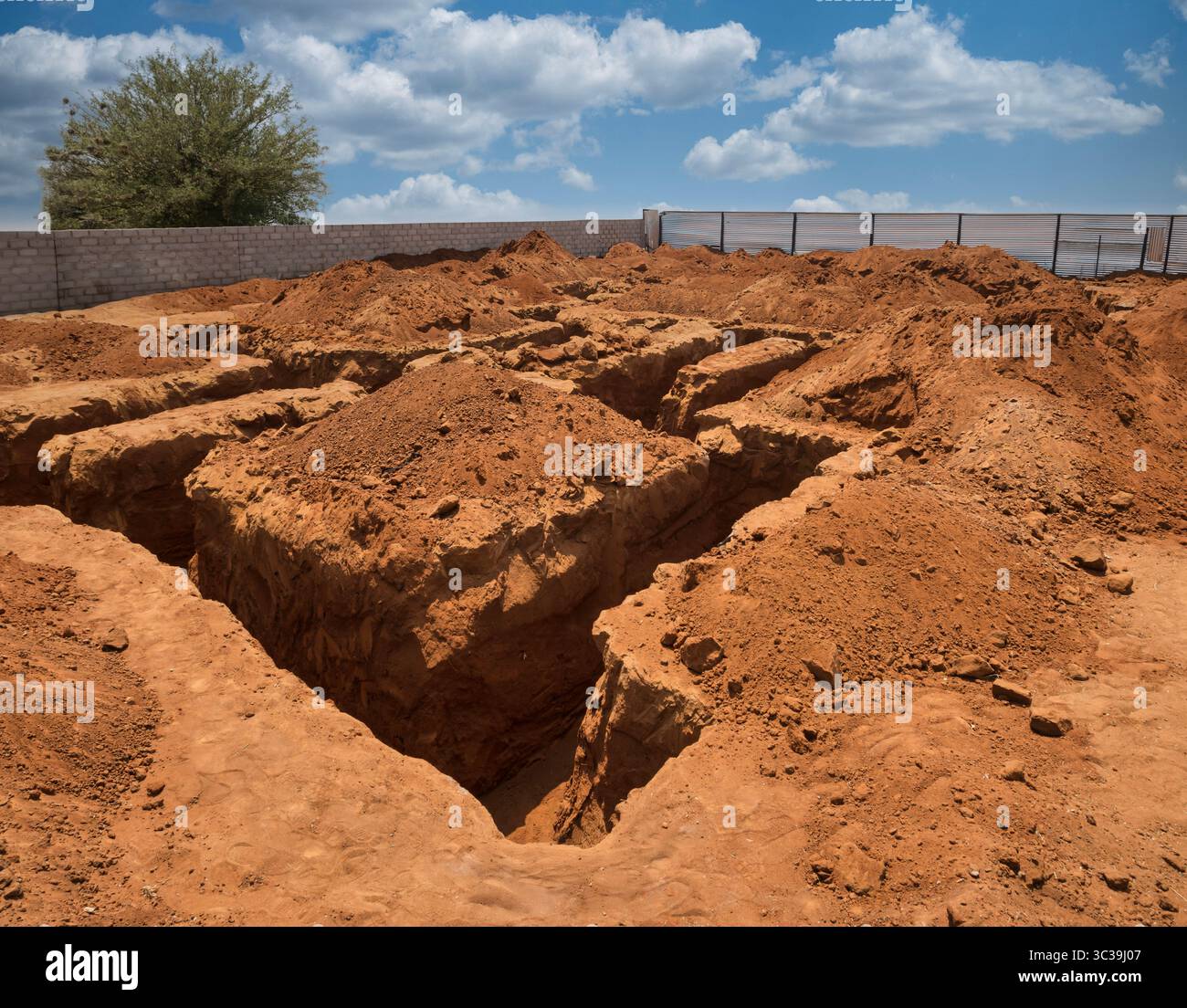 Scavo, fondazioni, con trincee per una grande casa, scavate in terreno rossastro, circondate da pali di sterrato e recinzioni metalliche, sotto il bricco Foto Stock