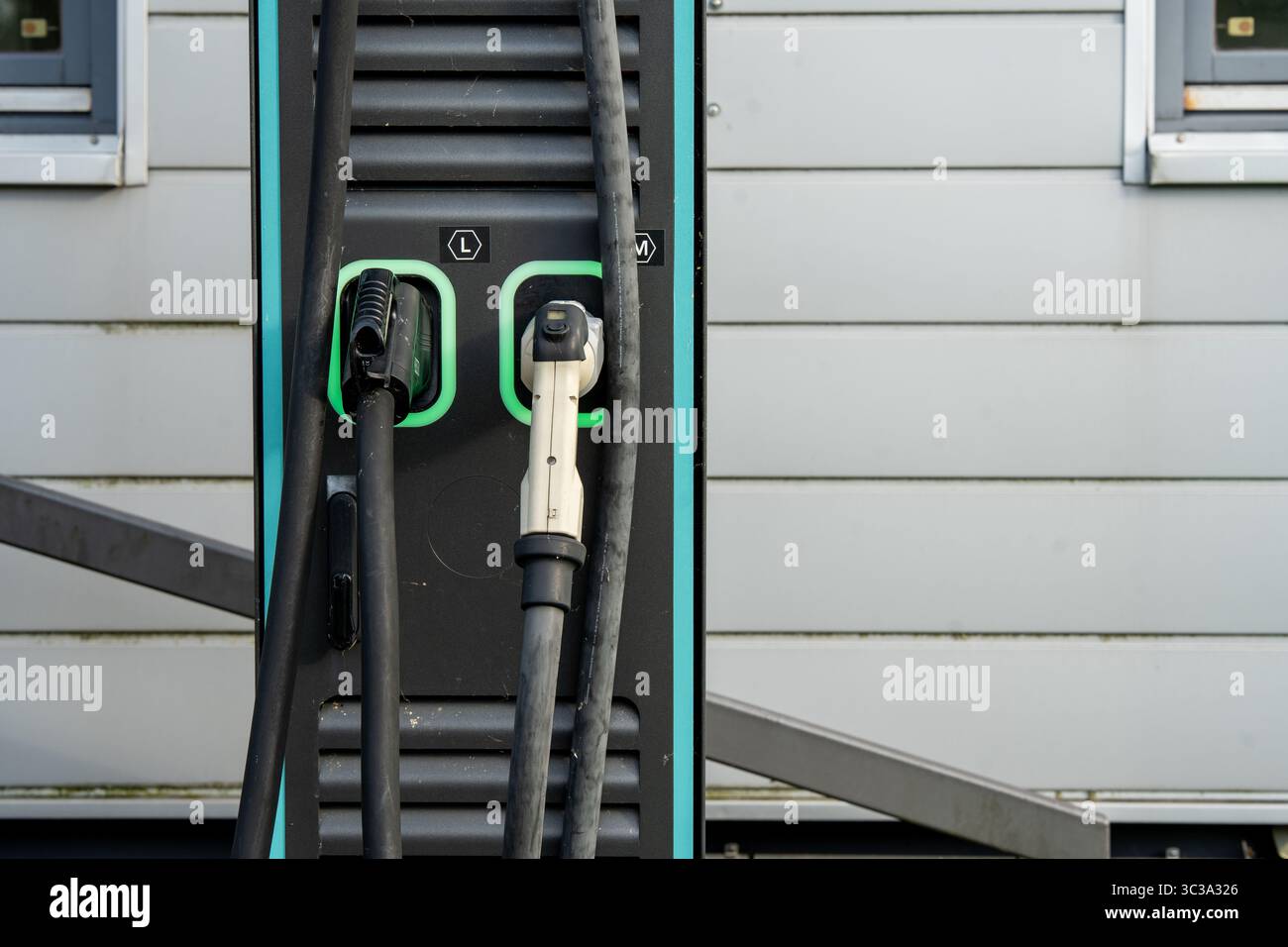 Stazione di ricarica per veicoli elettrici con due connettori: Primo piano dei cavi e delle prese di alimentazione EV moderni con linee LED verdi sul pannello nero Foto Stock