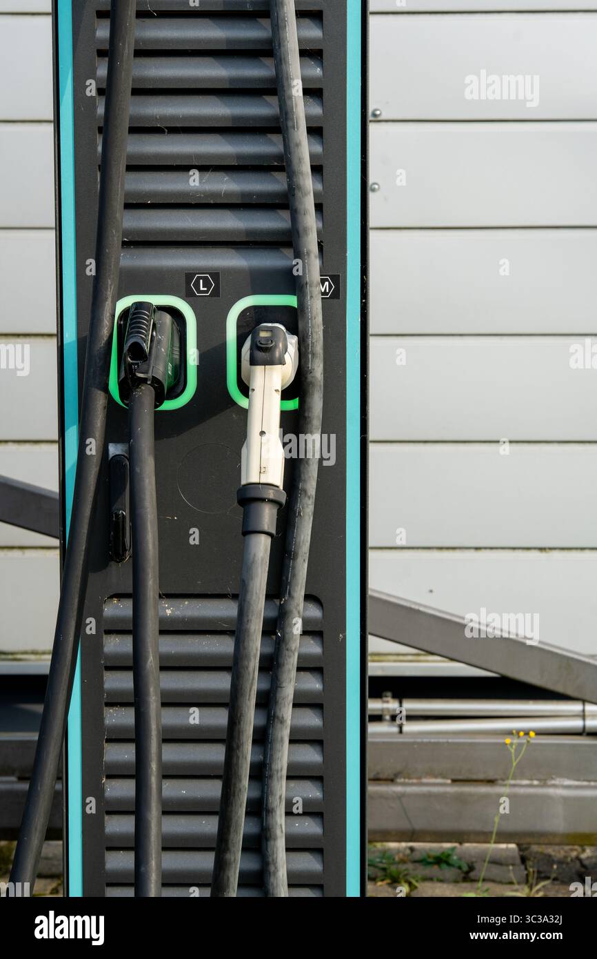 Stazione di ricarica per veicoli elettrici con due connettori: Primo piano dei cavi e delle prese di alimentazione EV moderni con linee LED verdi sul pannello nero Foto Stock