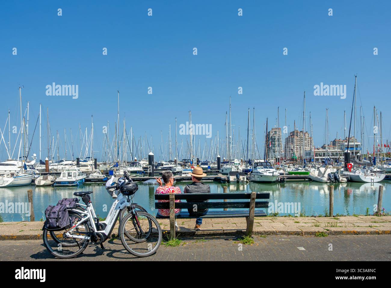 Due ciclisti che riposano sulla panchina e guardano le barche a vela nel porto turistico della località balneare Breskens lungo la Schelda occidentale, la Zelanda, i Paesi Bassi Foto Stock
