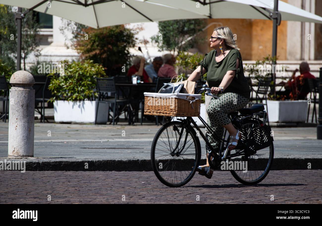 Donna con capelli biondi e occhiali da sole in bicicletta con cesto frontale. Foto Stock