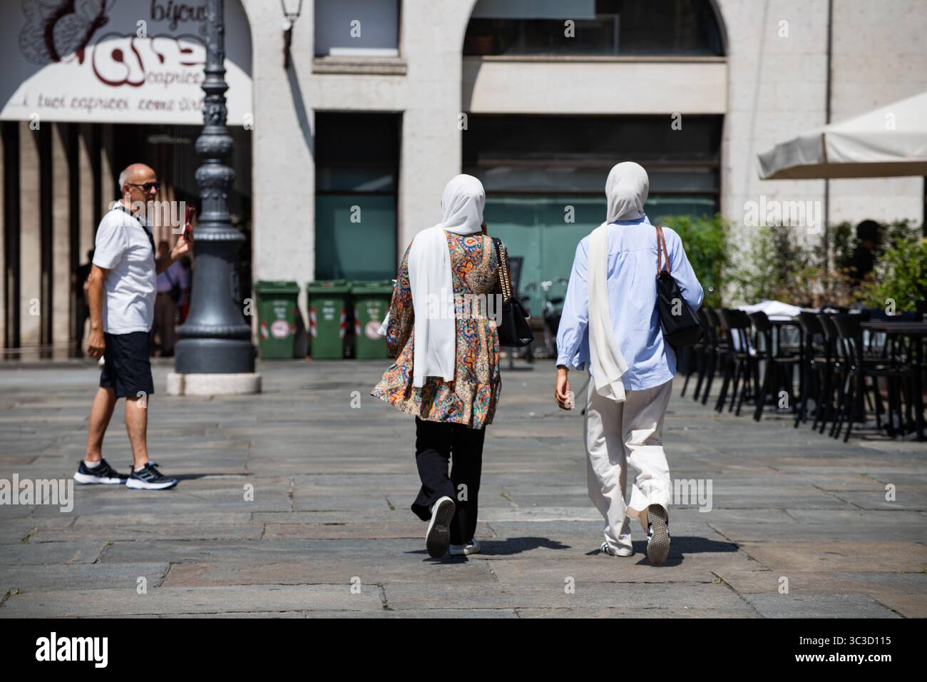 Due donne che indossano un velo che cammina su una piazza urbana acciottolata in una giornata di sole. Foto Stock
