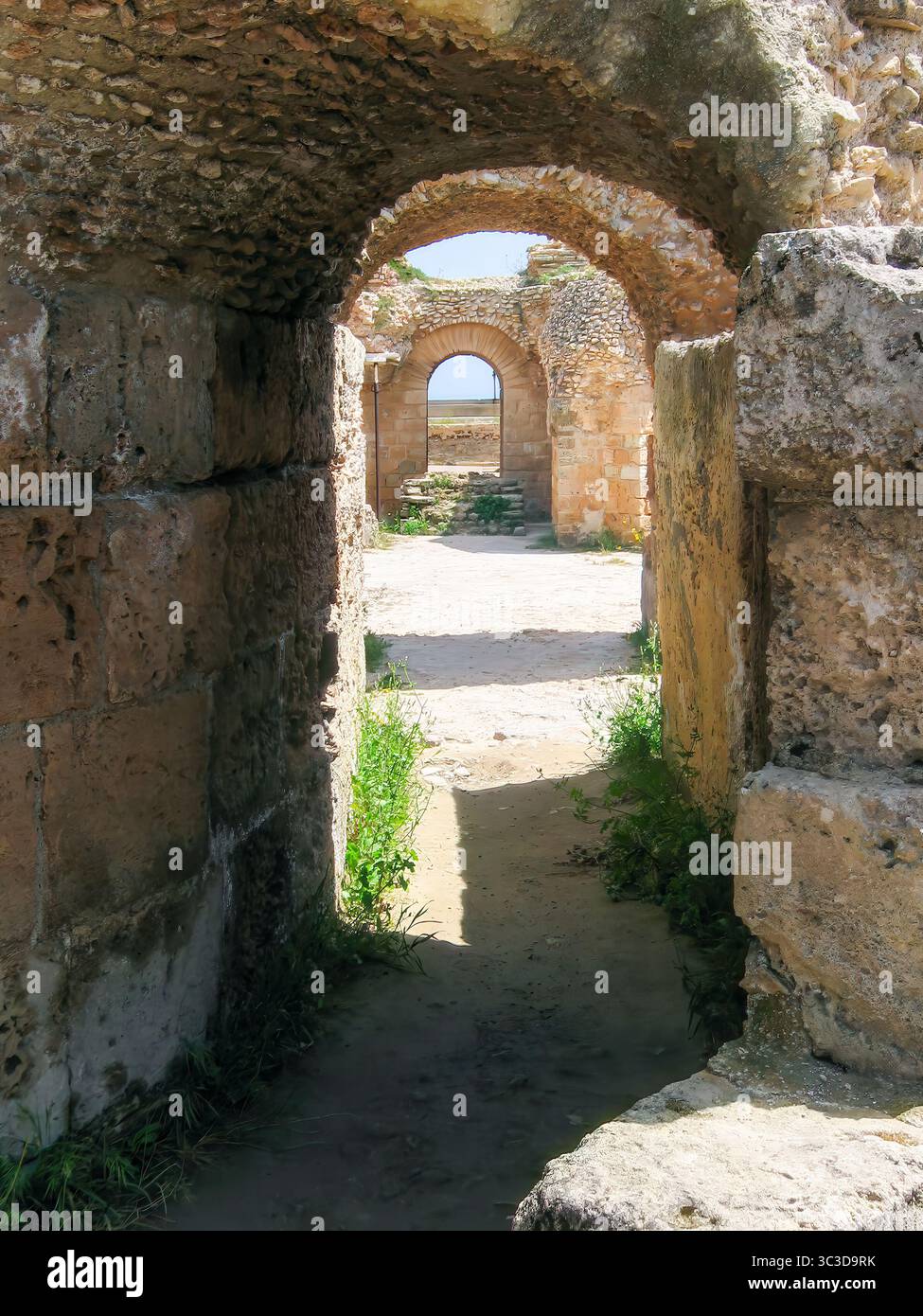 Arcata di pietra nelle rovine di Cartagine Romana, Tunisia. La calda luce del sole mette in risalto le antiche murature e conduce l'occhio attraverso l'architettura storica a strati Foto Stock