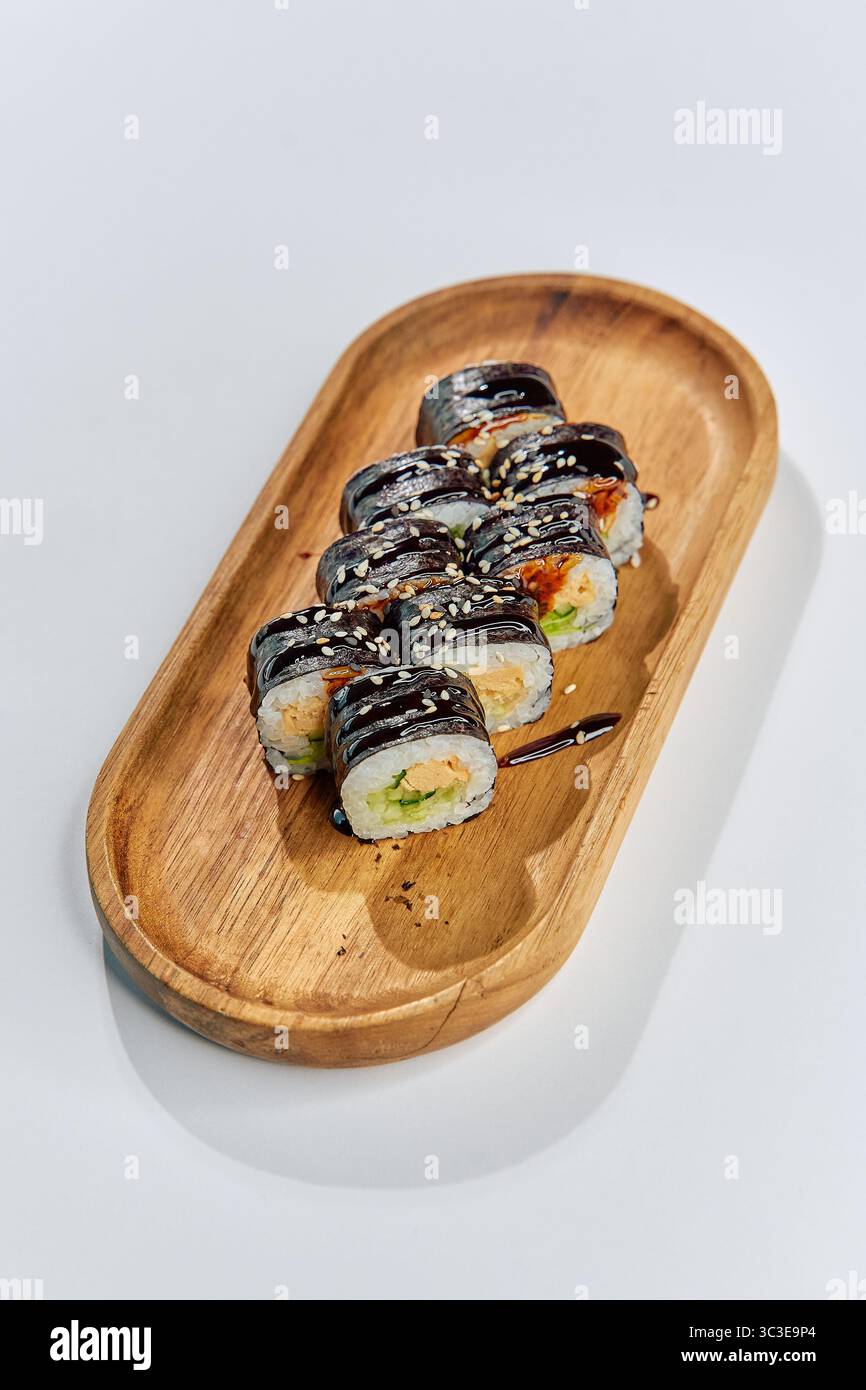 Deliziosi sushi roll disposti su un piatto di legno, con ingredienti freschi e colori vivaci, perfetti per un pasto gourmet o un pranzo informale Foto Stock