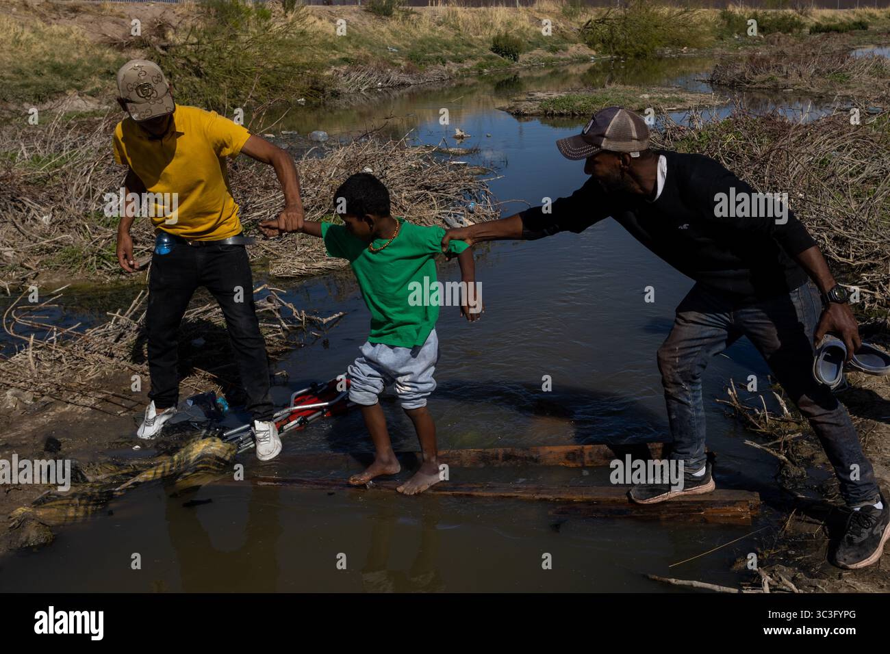 Due adulti assistono un bambino su un ponte precario a Ciudad Juarez, bypassando un sentiero allagato. Foto Stock