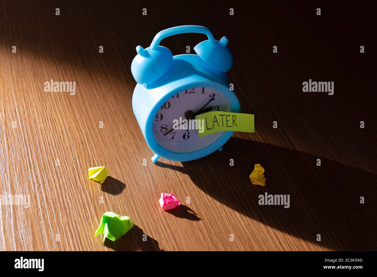 Una sveglia vintage su sfondo scuro con una nota "PIÙ TARDI". Concetto di procrastinazione, ritardo e attività dimenticate. Foto Stock
