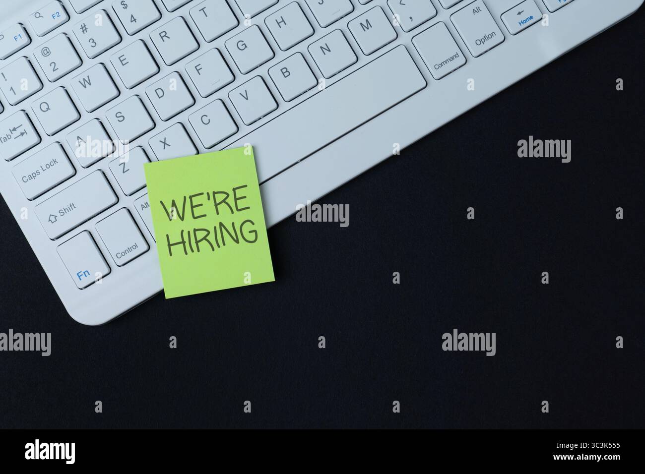 Una tastiera bianca per computer con una nota adesiva "STIAMO ASSUMENDO". Concetto di reclutamento, opportunità di lavoro e risorse umane. Copia spazio per il testo. Foto Stock