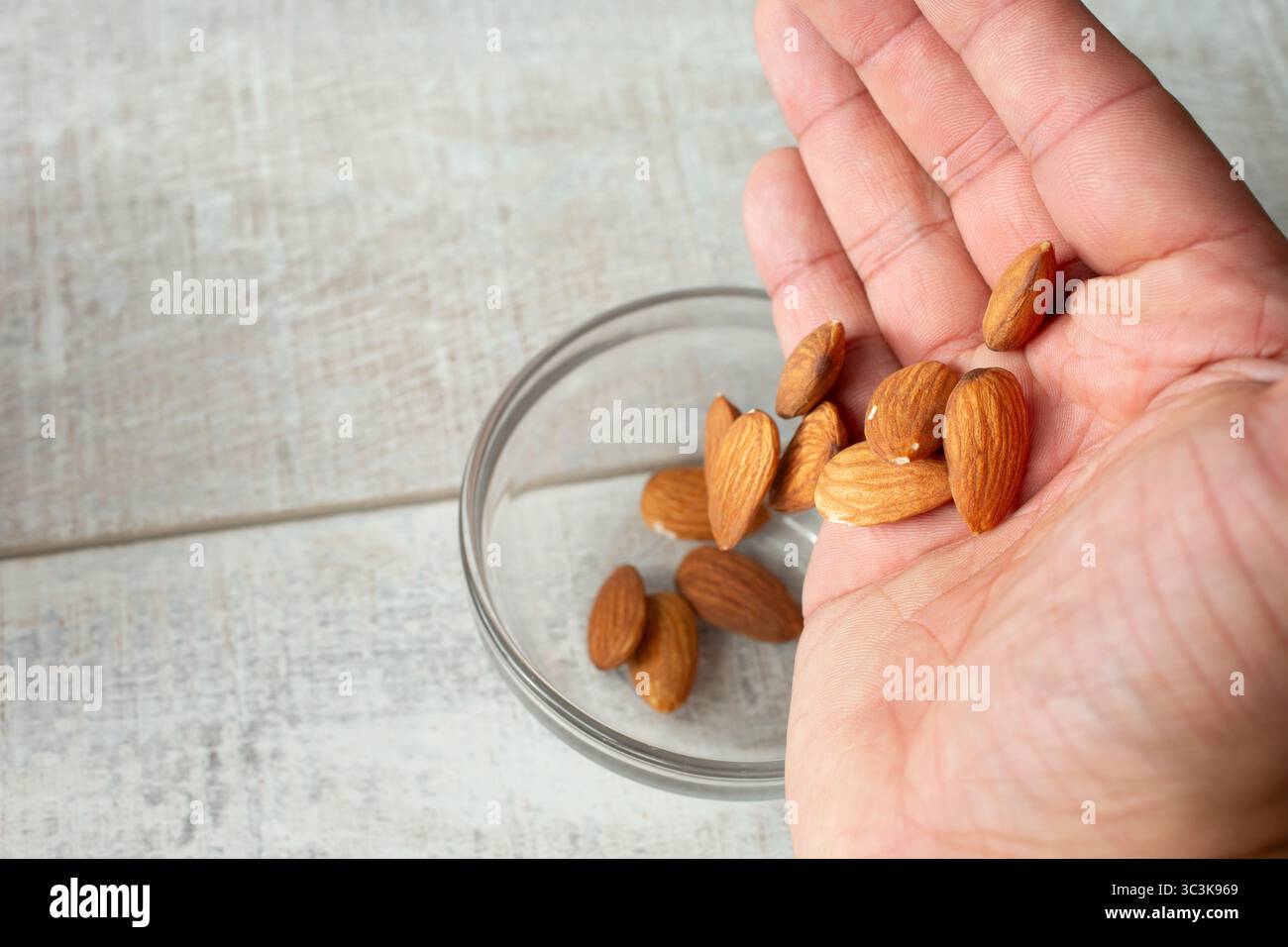 Una vista di una mano che fa cadere le mandorle in una tazza di bicchiere. Foto Stock