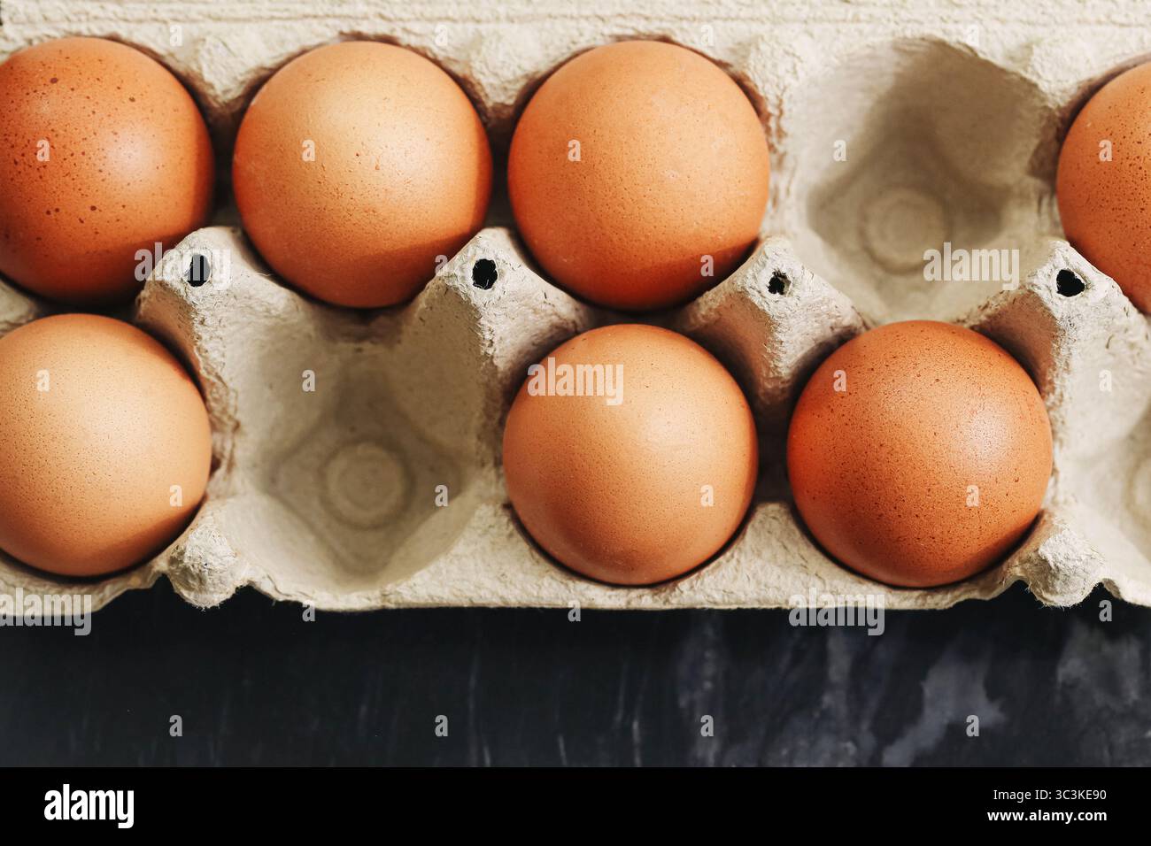 Brown le uova in cartone. Uova organiche in vassoio di carta riciclata su sfondo scuro. Cibo proteico sano. Primo piano sui prodotti agricoli. Confezione ecocompatibile. Foto Stock