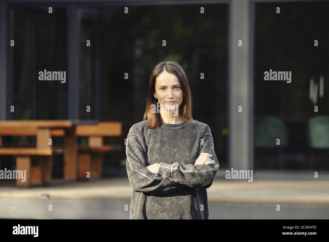 Una giovane donna con i capelli a spalla sta in piedi con le braccia incrociate all'esterno di un edificio elegante e moderno Foto Stock Una giovane donna con i capelli a spalla sta in piedi con le braccia incrociate all'esterno di un edificio elegante e moderno Foto Stock