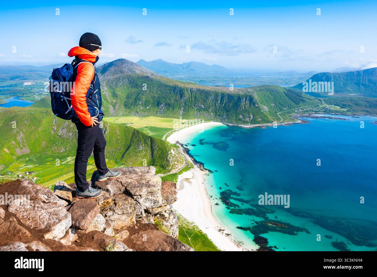 Escursionista femminile che gode di una vista spettacolare della spiaggia di Haukland con mare e montagne dal picco Mannen, Isole Lofoten, Norvegia Foto Stock