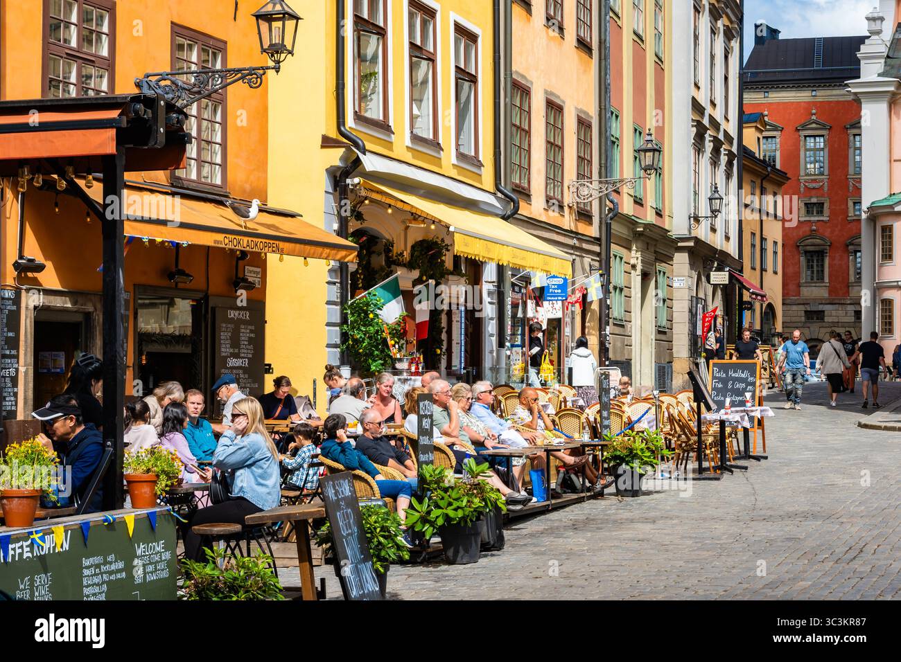 STOCCOLMA, SVEZIA - 30 giugno 2025: Case colorate in piazza Stortorget, nella città di Stoccolma, con persone sedute in ristoranti e caffetterie. Foto Stock