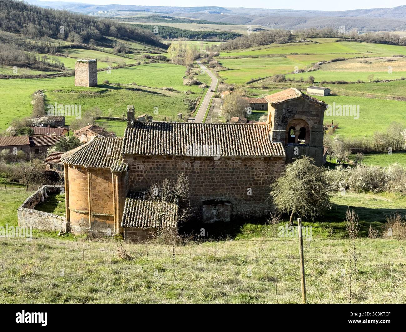 Storica chiesa romanica con pareti in pietra, tetto in piastrelle rosse e campanile annidato nella campagna di Palencia. Foto Stock
